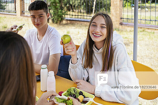 Happy girl having fresh fruit sitting at table in schoolyard