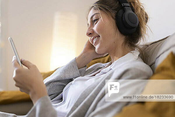 Happy woman wearing wireless headphones using smart phone at home