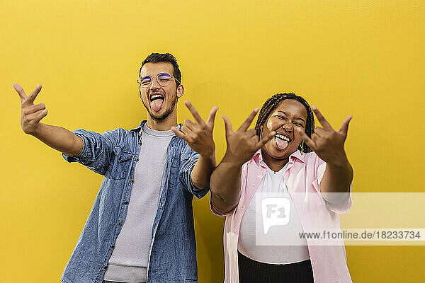 Cheerful young couple gesturing horn sign in front of wall
