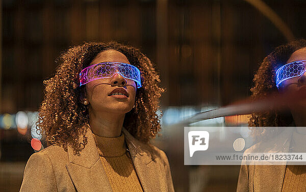Young woman with curly hair wearing blue and pink smart glasses at night