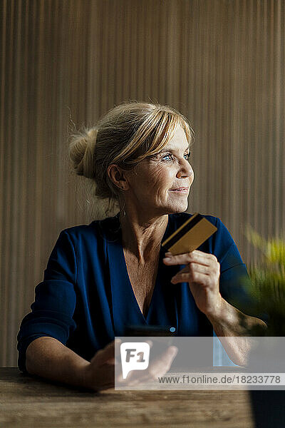 Smiling thoughtful businesswoman with smart phone and credit card in office