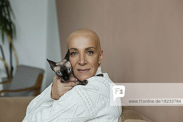 Mature hairless woman embracing Sphynx cat on sofa