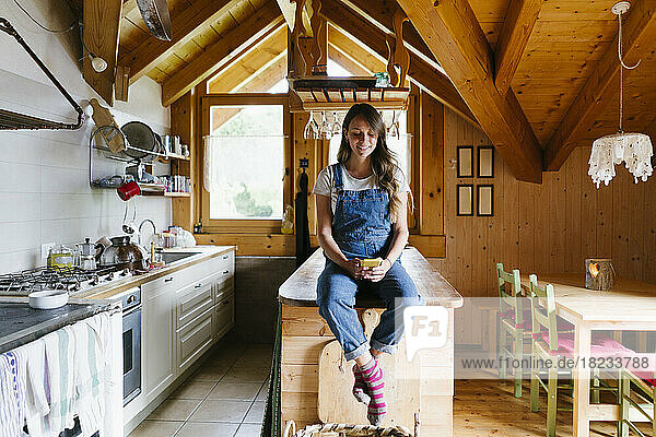Smiling woman using smart phone sitting on kitchen island