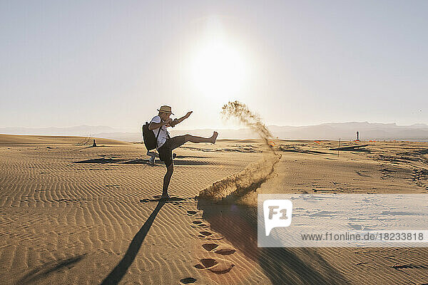 Playful man kicking sand on beach at sunset