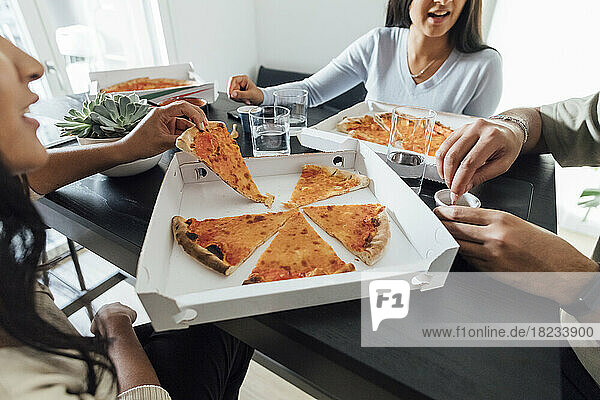 Hände von Frauen und Männern am Pizzakarton auf dem heimischen Tisch