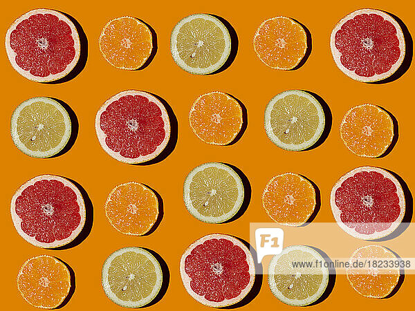 Pattern of halved lemons  grapefruits and tangerines flat laid against orange background