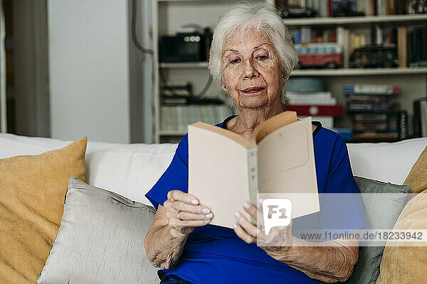 Ältere Frau liest zu Hause auf dem Sofa ein Buch