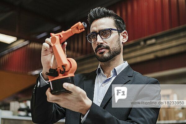 Businessman wearing eyeglasses examining robotic arm at factory