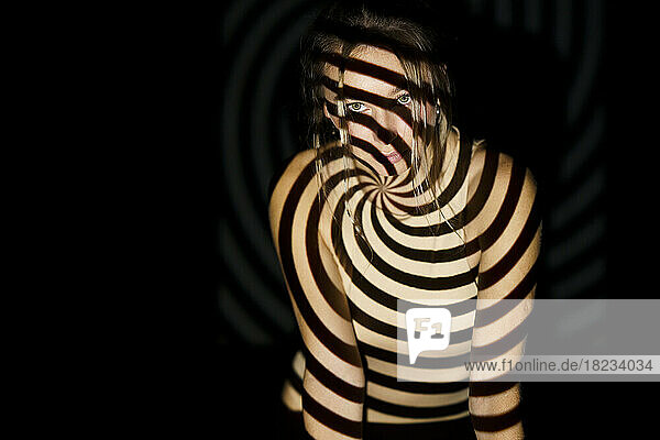 Frau mit spiralförmig beleuchtetem Muster auf dem Körper vor schwarzem Hintergrund
