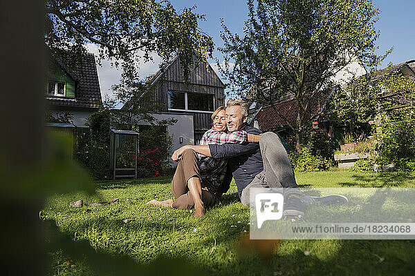 Mature woman hugging man sitting on grass in backyard