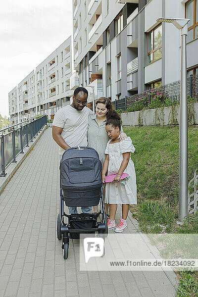 Family with baby stroller standing at footpath
