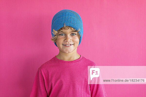 Smiling boy wearing blue knit hat against pink background