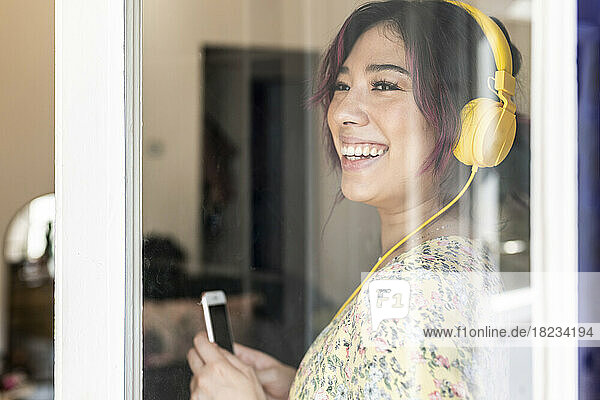 Happy young woman wearing headphones seen through glass window