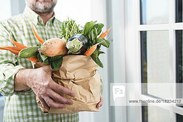 Mature man holding paper bag with fresh vegetables at doorway