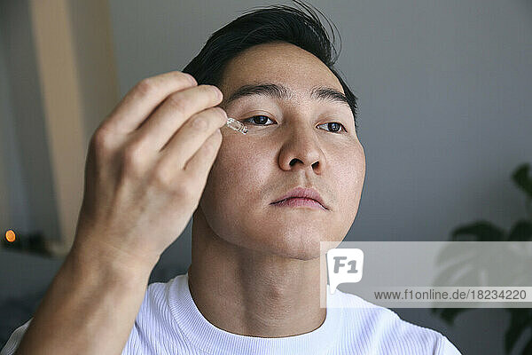 Young man applying face serum at home