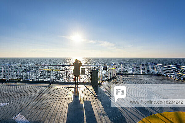 UK  Scotland  Lone woman looking at setting sun from afterdeck of moving ferry