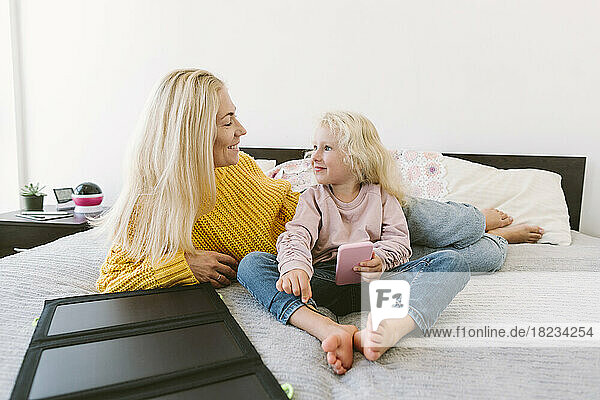 Happy mother and daughter sitting on bed at home