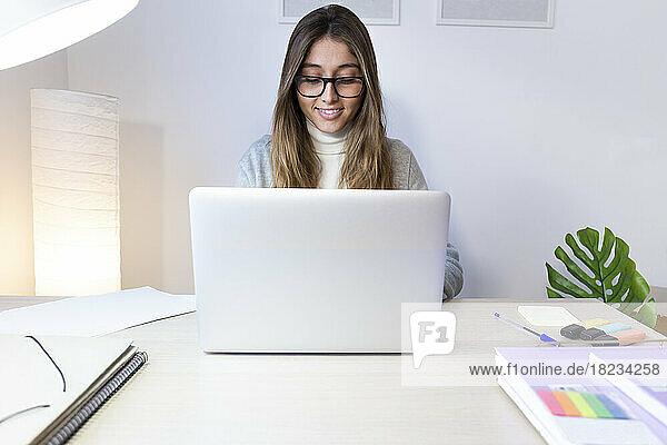 Happy young woman studying on laptop at desk