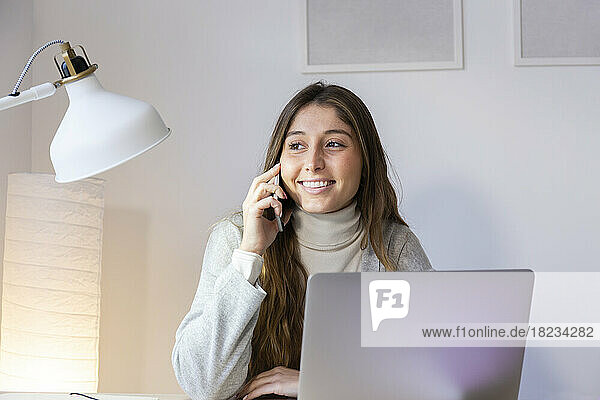Smiling young woman talking on smart phone at home