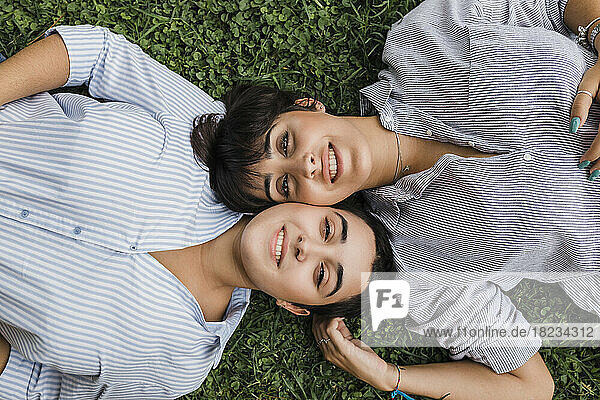 Lesbian couple lying with cheek to cheek on grass