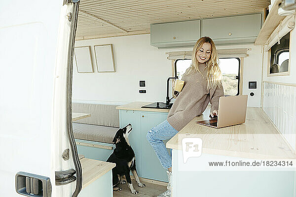 Happy young digital nomad using laptop with dog in motor home
