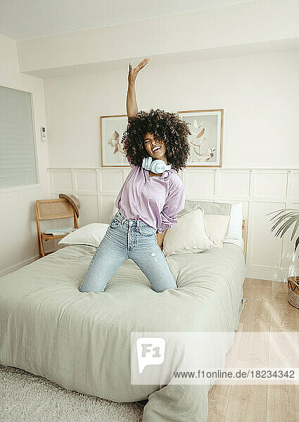 Happy young woman with hand raised dancing on bed at home