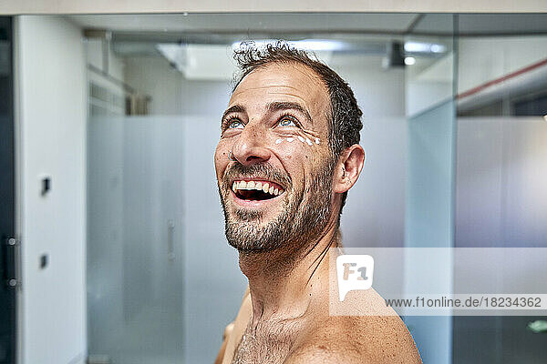 Cheerful man with moisturizer cream on face in bathroom at home