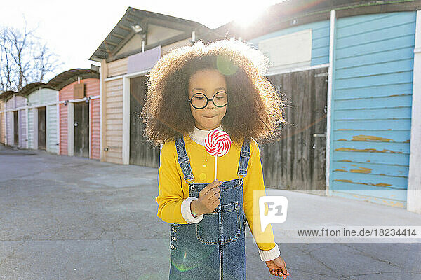 Girl looking at lollipop near beach huts on sunny day