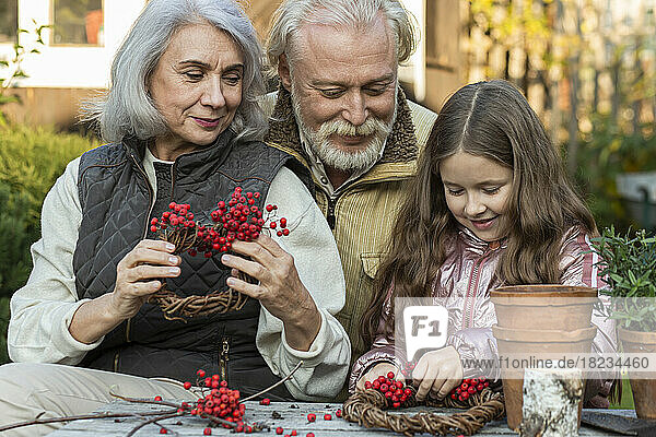 Grandparents and granddaughter sitting at garden table crafting with mountain ash