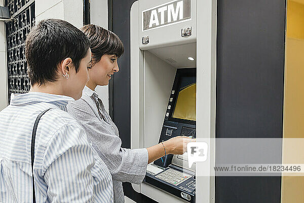 Junge Frau mit Freundin benutzt Geldautomaten