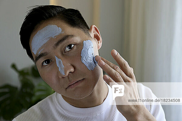 Young man applying mask on face at home