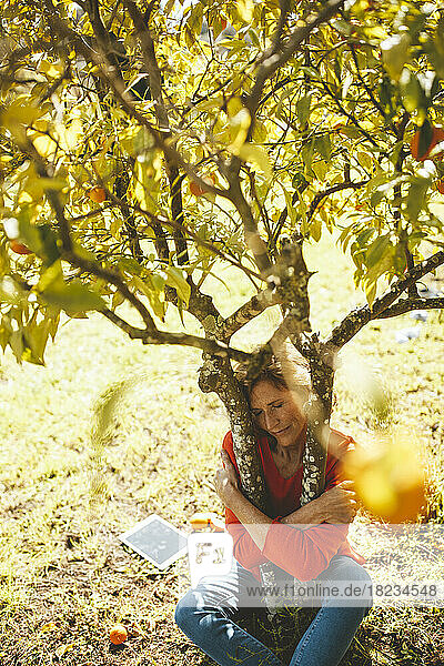 Mature woman with eyes closed hugging orange tree