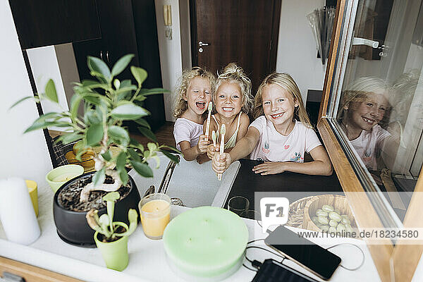 Happy girls showing wooden toothbrushes in the kitchen