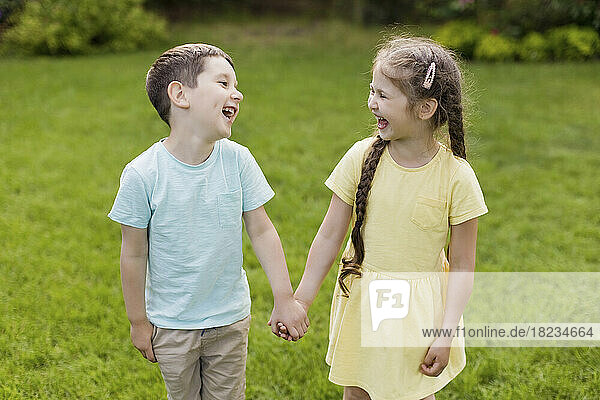 Brother and sister holding hands and laughing together in back yard
