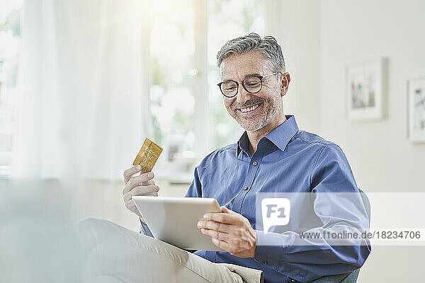Happy man with credit card doing online shopping through tablet PC at home