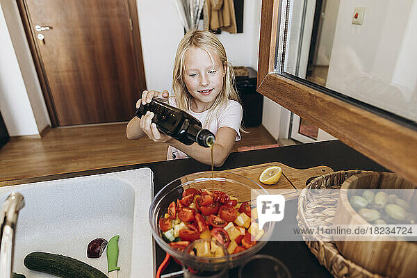Mädchen bereitet in der Küche einen Salat zu und gießt Öl in eine Schüssel