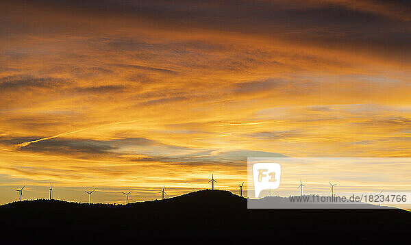 Moody sky over silhouettes of wind farm turbines at sunset