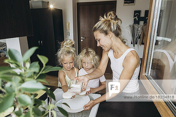 Woman with daughters washing dishes with salt in the kitchen