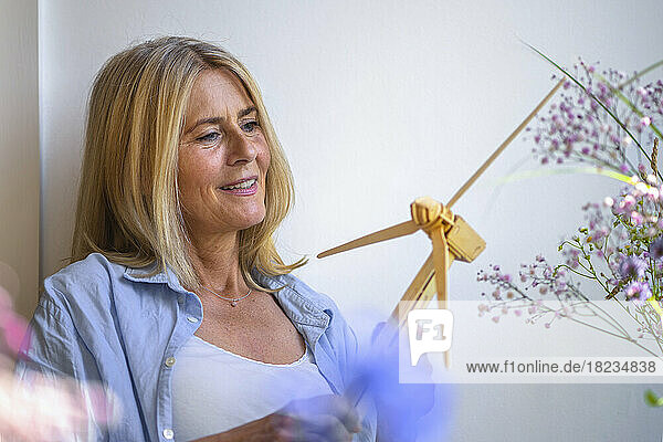 Mature woman looking at wind turbine model in front of wall at home