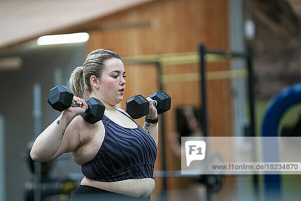 Overweight woman doing exercise with dumbbells in gym