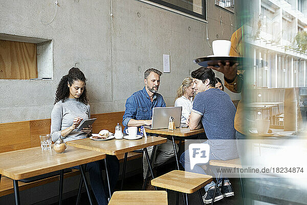 Customers using wireless gadgets sitting at table in coffee shop