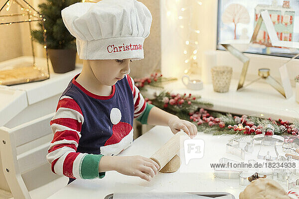 Boy wearing chef's hat rolling gingerbread dough at kitchen counter