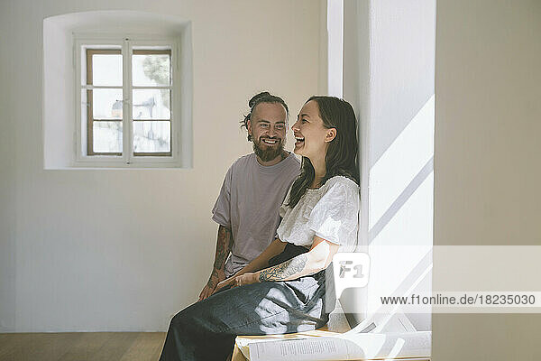 Glücklicher Hipster-Mann mit Freundin sitzt zu Hause auf einem Tisch vor der Wand