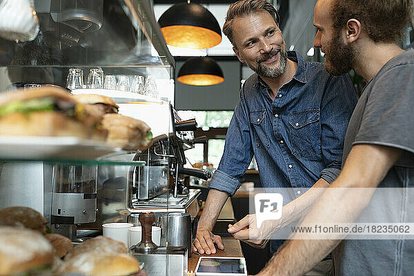 Smiling cafe owner talking to barista in coffee shop