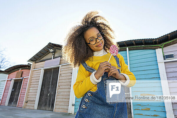 Smiling girl holding lollipop in front of beach huts