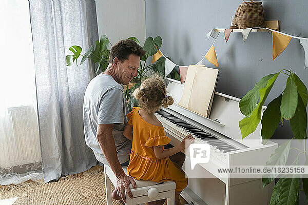Father teaching daughter piano at home