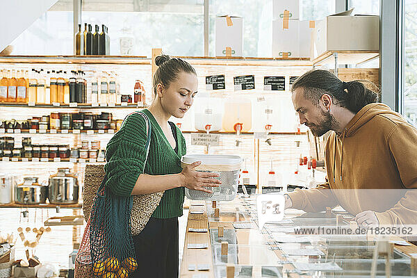 Man reading labels on counter by woman with container in shop