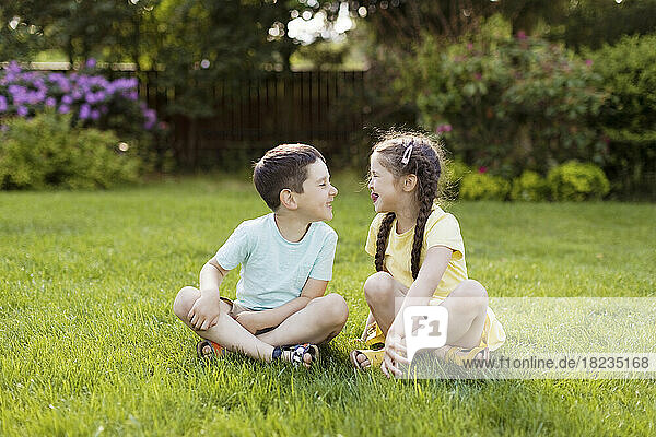 Happy brother and sister sitting on grass in garden