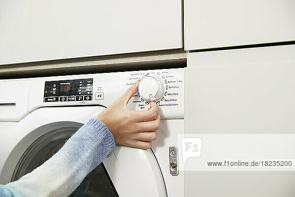 Hand eines Mädchens  das den Knopf an der Waschmaschine zu Hause einstellt