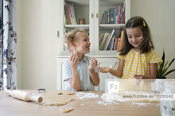 Fröhliche süße Mädchen bereiten zu Hause Kekse mit Teig auf dem Tisch zu